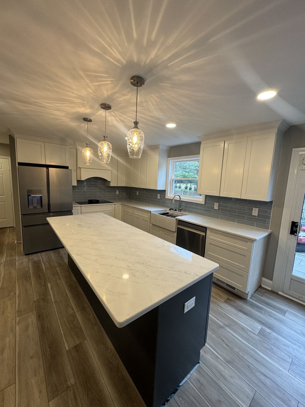 Finished white shaker kitchen with a navy island, quartz top, pendant lights and wood-look floor