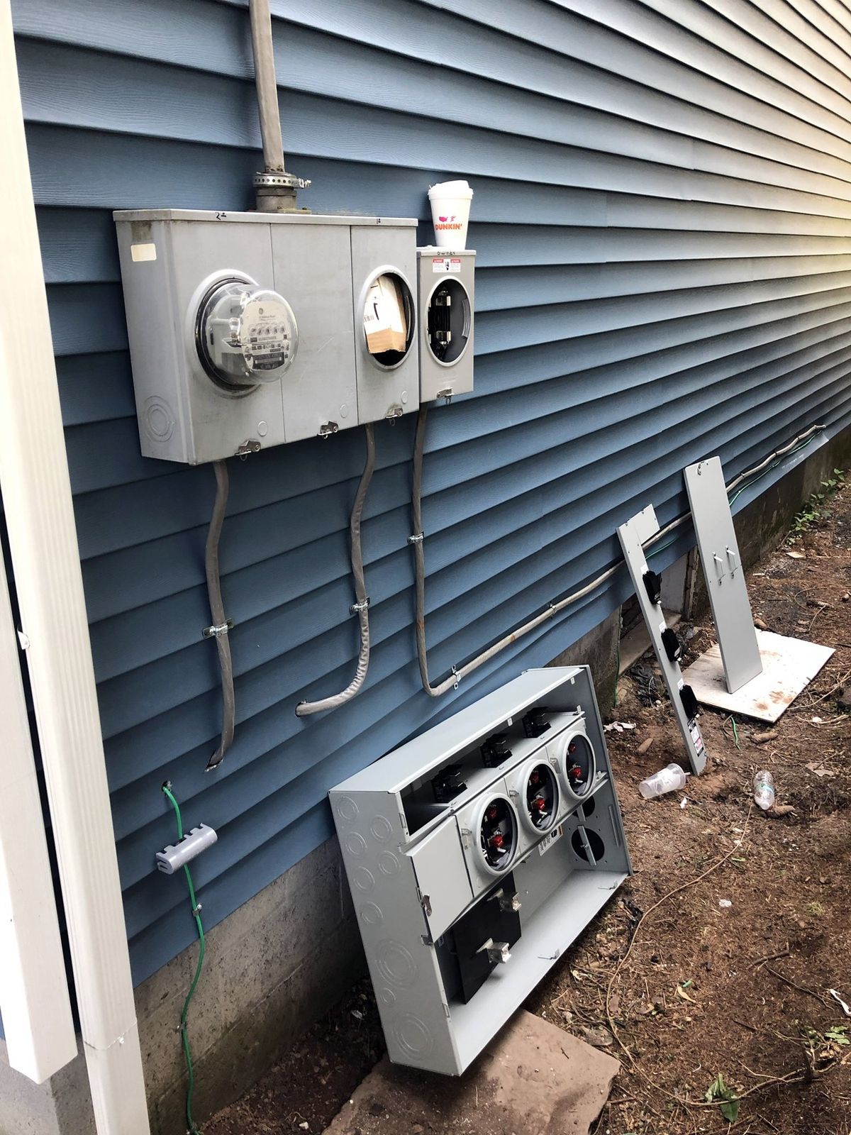 Old separate meter sockets on a house wall, with the new multi-meter unit on the ground ready to install