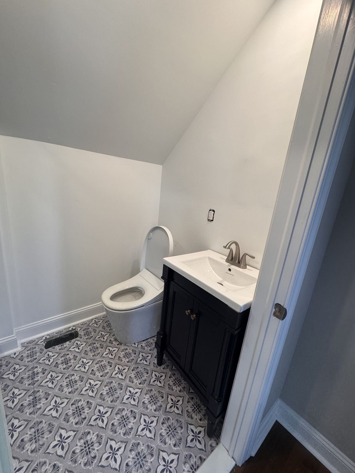 The same room finished as a half bath with patterned tile, vanity and toilet